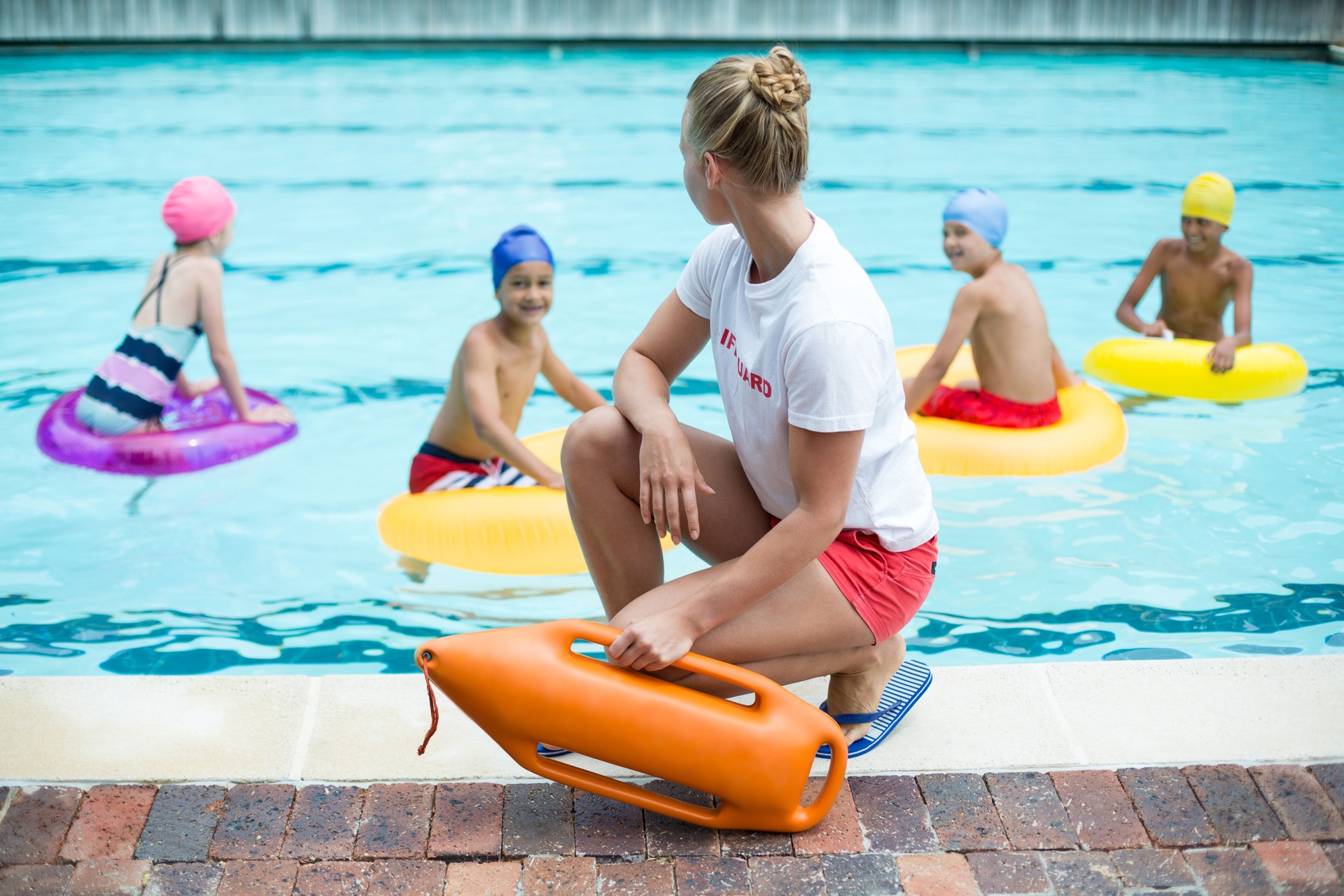 Lifeguard holding rescue can while children swimming in pool